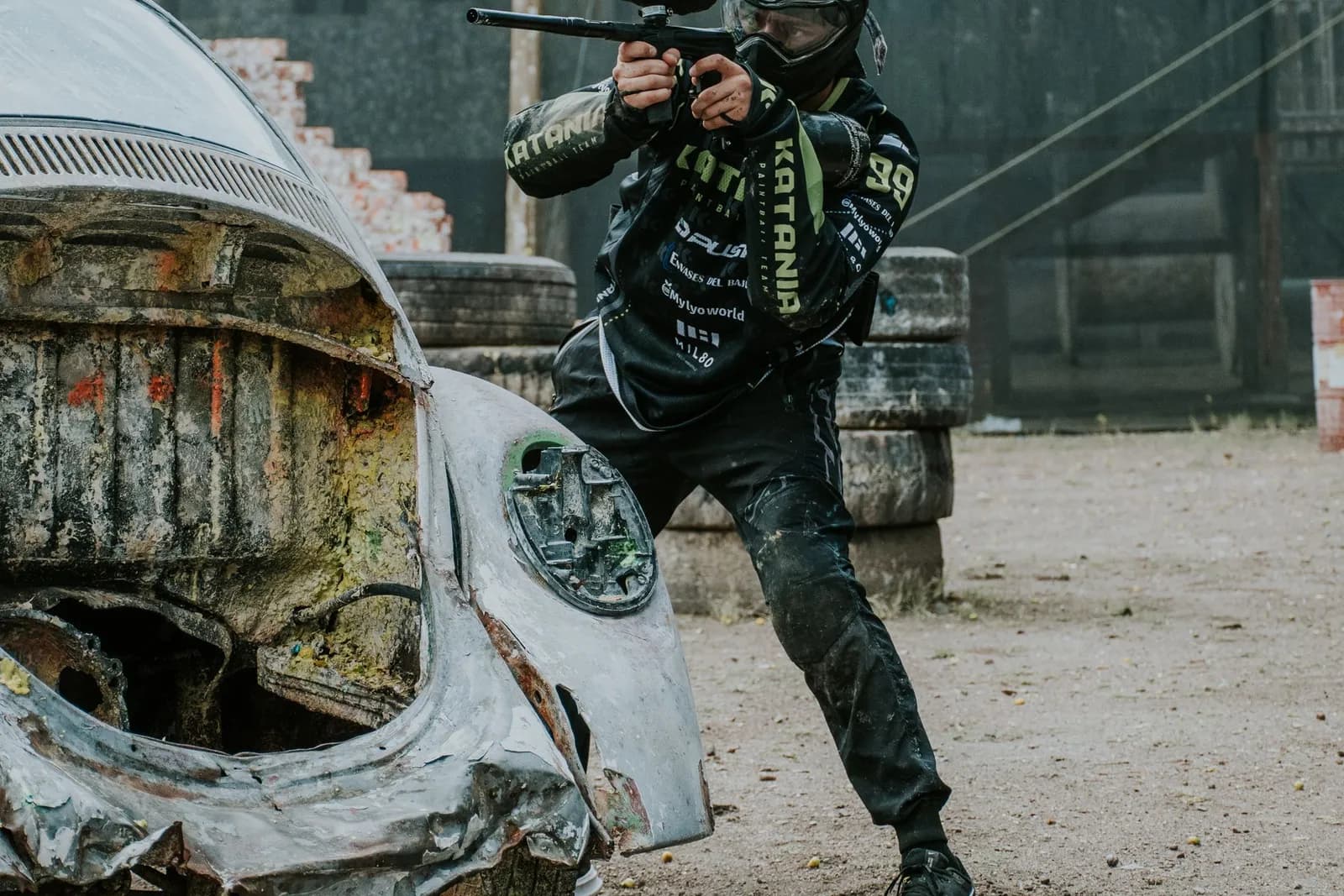 Joueur de paintball tirant à l'abri d'une vieille voiture rouillée sur un terrain de scénario